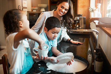 年轻快乐的混血母亲和她的儿子和女儿在家里的厨房里洗碗 弟弟妹妹帮妈妈洗碗 家庭保持他们的房子干净图片