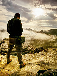 摄影师检查照相机显示的相机 男人留在悬崖上冒险相片背包风景远足者手机风光运动员人士帝国图片