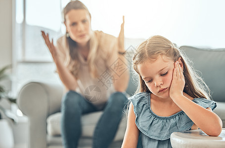 悲伤的白人小女孩坐在客厅里 感到沮丧 而她的母亲在她身后大喊并举起双手 年轻可爱的女儿在让父母失望后感到不安图片