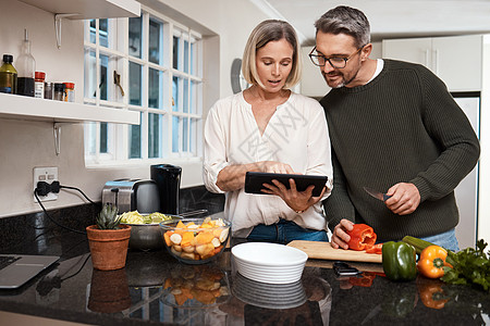 我想试试这个食谱 成熟的夫妇在家里一起做饭时 用数字平板电脑做饭图片