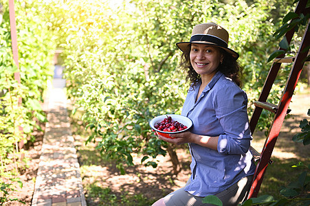 美丽的女人 生态农民 笑着牙齿的笑脸 看着相机 拿着一碗新鲜采到的成熟樱桃图片