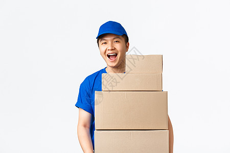在线购物 快速运输概念 穿着蓝色快递制服的乐观微笑的亚洲送货员拿着带订单的箱子 把包裹送到客户家 站在白色背景中欢快地站着服务邮图片