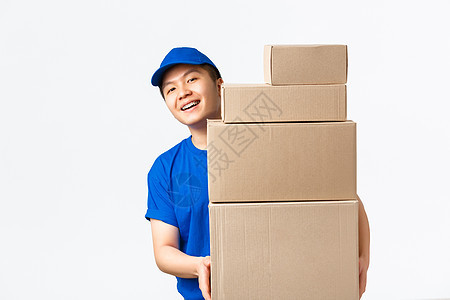 在线购物 快速运输概念 身穿蓝色快递制服 面带微笑 快乐的亚洲送货员 在装着客户订单的箱子后面看 把包裹送到客户家 白色背景图片