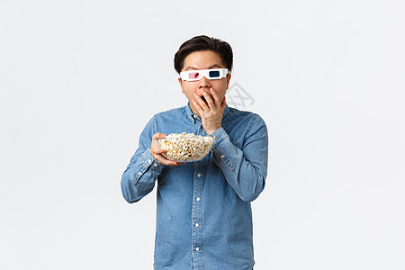 休闲 生活方式和人们的观念 惊讶的亚洲人戴着 3d 眼镜嚼着爆米花兴奋地看着电视 在宽屏上看电影 去电影院 站在白色背景图片