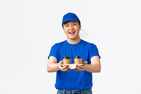 友好 笑笑的亚洲人送货员穿蓝信使制服 向有喜悦表情的客户提供咖啡杯 站立白底背景图片