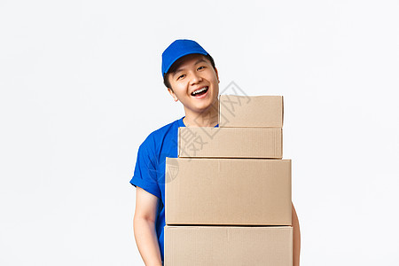 在线购物 快速运输概念 穿着蓝色快递制服的乐观微笑的亚洲送货员拿着带订单的箱子 把包裹送到客户家 站在白色背景中欢快地站着工人邮图片
