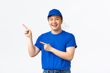 穿着蓝色制服的快乐的年轻亚洲男性快递员指着左上角的手指 关于船运公司的广告 包裹运输 逗人喜爱的送货员促进某事工人工作购物销售导图片