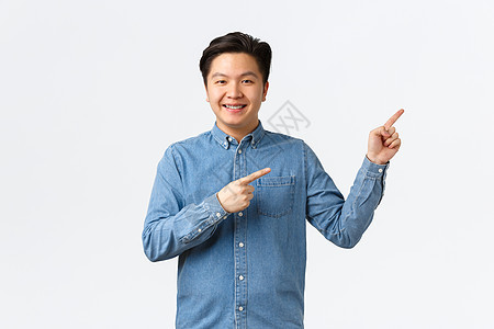 笑得开朗的亚洲年轻人 戴着蓝色衬衫的牙套 指着右上角骄傲而自信 显示链接或发布公告 站在白色背景图片