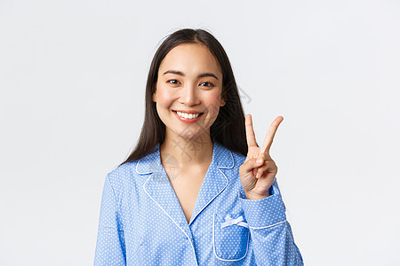 穿着蓝色睡衣的快乐迷人亚洲女性的特写镜头 她露出二号和微笑的白牙 解释主要规则或下达命令 站在白色背景上很高兴图片
