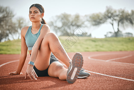 一位年轻的运动员在跑步的轨道上拉伸她的身体 他把身体拖到赛道上图片
