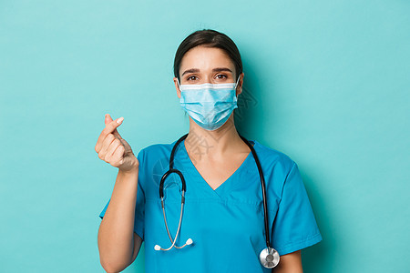 covid-19 的概念和检疫概念 身穿磨砂膏和医用面具的开朗美丽女医生 显示心脏标志 站在蓝色背景上图片