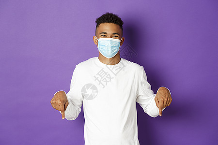 冠状病毒 检疫和生活方式的概念 身戴医学面具的非洲美籍男子展示宣传 用手指向徽标和微笑 站在紫色背景上站立着图片
