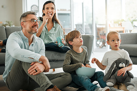 正在看我们最喜欢的电影 一个年轻家庭在家里一起看电视的节目呢图片