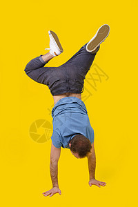 穿着休闲服的年轻男子倒立在镜头前 摆出黄色背景的姿势 时尚的外观时髦的人 黄色背景中用手行走的运动青年图片