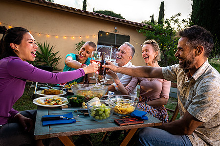 亚洲女人在日落的烧烤花园晚宴上 喝着葡萄酒 笑和玩乐 来庆祝祝酒图片