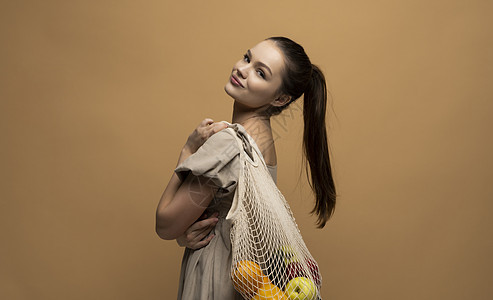 有棉花可再使用的网状袋装满水果的年轻黑发妇女 在免费塑料杂货店购买没有塑料包装的购物图片