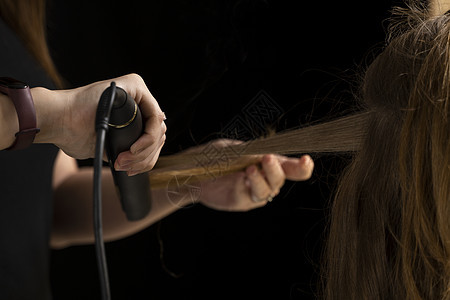 一个美容师的手 与卷轴铁做发型 在专业美容院为卷发女孩图片