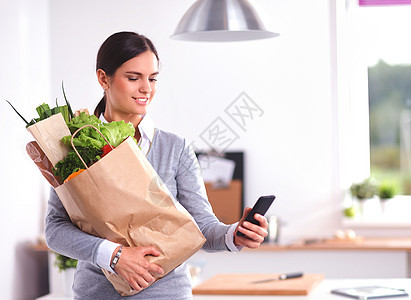 青年妇女拿着杂货袋和蔬菜 站在厨房里 女水果胡椒顾客饮食营养市场保健烹饪微笑食物图片