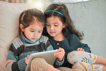 一个数字保姆 两个年轻的妹妹 在家里沙发上一起用数码平板电脑玩耍图片