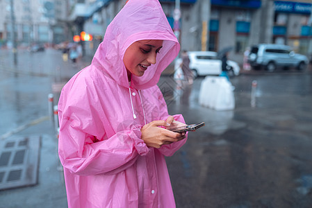 一个穿雨衣的年轻女人 看着智能手机女士成人头发皮肤天气城市下雨喜悦假期女性图片