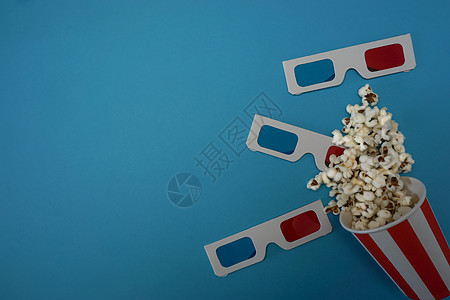 爆米花被倒在蓝色背景上 在背景上是看电影的眼镜图片