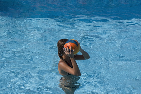 年幼的棕色女孩拿着球 在游泳池里玩水排球图片