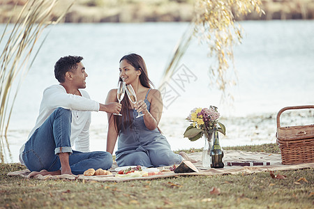 一对年轻的情侣坐在一起 喝着香槟的酒 在野餐约会中举杯祝酒 我和他共度难关图片