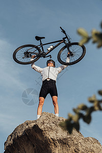职业男性赛事名单 在站在山顶 天空在背景上时 用自行车举起手来车轮骑士运动头盔冒险踪迹娱乐铁人眼镜运动员图片