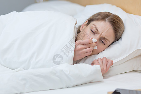 近距离照片显示 一名生病的妇女躺在家中床上的毯子下 鼻子破鼻和寒冷发烧焦虑感染手帕女孩眉头长椅流感组织卧室图片