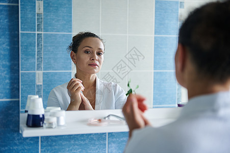 浴室镜子里的倒影是一位平静的女人 她用润肤霜按摩双手 呵护双手皮肤图片