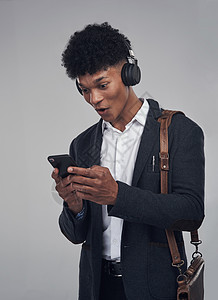 电影演播室拍摄一名年轻商务人士在灰色背景下使用智能手机和耳机的青年商务人士 他被拍到了一张照片图片