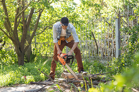 一个带电锯的男人 从旧树上拔除园圃中的植物 收获木柴樵夫危险机器头盔木头工人链锯工作日志男性图片