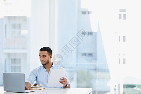 管理他的商业投资 一个年轻商务人士在办公室用笔记本电脑工作时 正在办理文书手续的生意图片