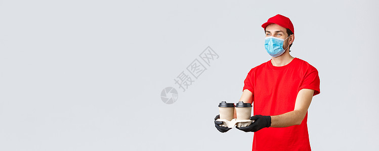 外卖 食品和杂货配送 covid19 非接触式订单概念 穿着红色制服 面罩和手套的愉快的快递员 给顾客发咖啡 站在灰色背景互联网图片