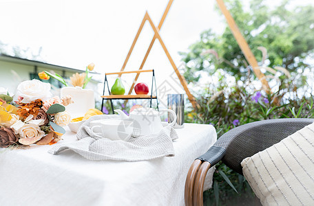 花园里桌子上的咖啡杯和鲜花花束 下午茶的概念 家庭户外家具 藤椅和桌子与复古风格的白色桌布 露台上舒适的椅子和桌子玻璃房子早餐休图片