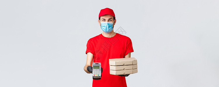 送餐 应用 网上杂货 非接触式购物和 covid19 概念 身着红色制服 面罩和手套的友好快递员 拿着订购的披萨盒 并给客户 P图片