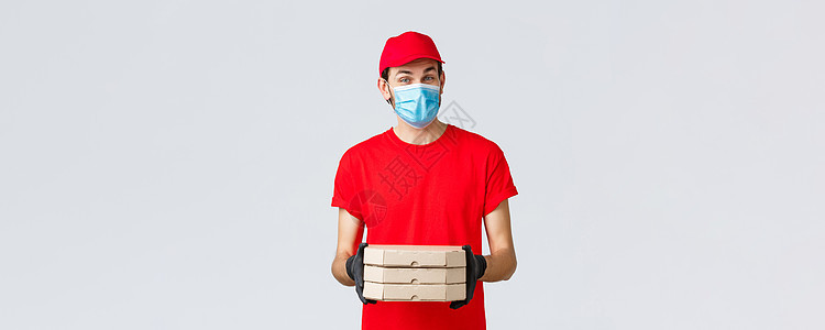 提供食品 申请 在线杂货 不接触的购物和共食19概念 穿红色制服的畅快信使携带披萨盒 戴面罩和橡皮手套 发出衣着订单员工食物后勤图片