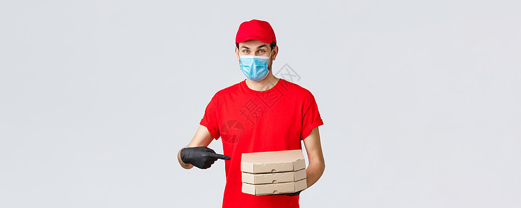 送餐 应用 网上杂货 非接触式购物和 covid19 概念 身着红色制服 面罩和手套的快乐快递员用手指指着披萨盒 送到客户家邮递图片