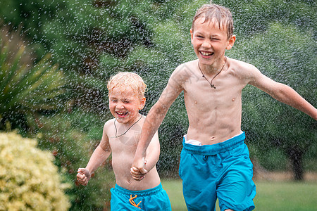 孩子们在炎热的夏天玩水 带花园洒水装置的儿童 户外乐趣 男孩们在水滴下的田野上奔跑晴天男生假期童年场地公园洒水器院子飞溅跑步图片