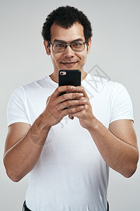 一位英俊的年轻人用他的手机站在灰色背景之下 他却站着不动地使用手机图片