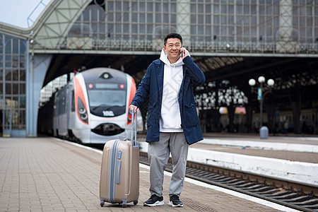 在火车站的亚洲男商务人士 玩着在电话里聊天吗企业家说话车站男人商务讲话平台微笑运输游客图片