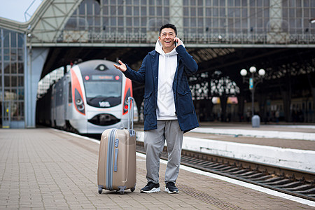 在火车站的亚洲男商务人士 玩着在电话里聊天吗人士说话讲话微笑旅行平台大厅游客手机男性图片