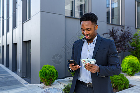 非洲裔美国商务人士站在街上 现代建筑显示赢得丰厚的收益库存金融男性管理人员支付货币企业家基金密码办公室图片