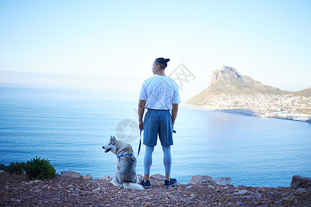 停下来欣赏风景 一个面目全非的年轻人和他的宠物哈士奇清晨在山上徒步旅行时的后视照片图片