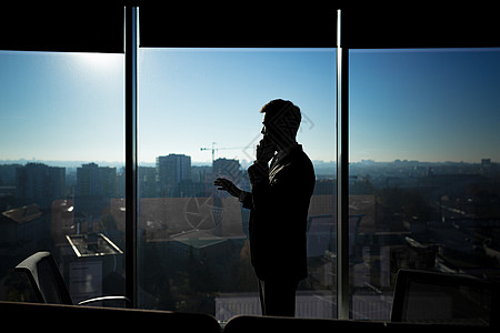 建筑剪影在窗户背景的现代办公室里 一个商务人士的剪影 一个男人在电话里说话雇主日落男人地平线商业企业家老板奢华经理建筑背景