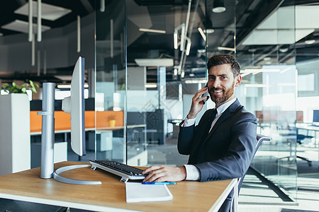 成功的商务人士在现代办公室工作 在电脑前 一个快乐的人看着镜头微笑 在电话里聊天图片