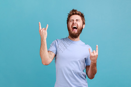 穿着蓝色T恤的男人展示摇滚和滚动手势 重金属标志享受最喜爱的音乐 在派对上图片
