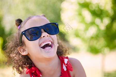 你会发现我在阳光明媚的一面很开心 一个可爱的小女孩在公园里戴着墨镜图片