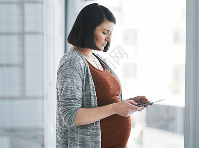 回到企业 但首先给我的OBGYN发条短信 一个怀孕的年轻女商务人士 在现代办公室使用数码平板电脑图片