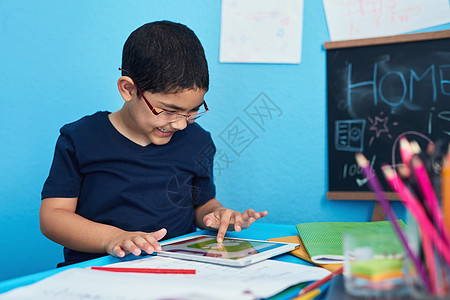 一个可爱的小男孩用数字平板电脑 完成在书桌的学校任务 他需要你帮忙吗? 我不需要他来做这个图片